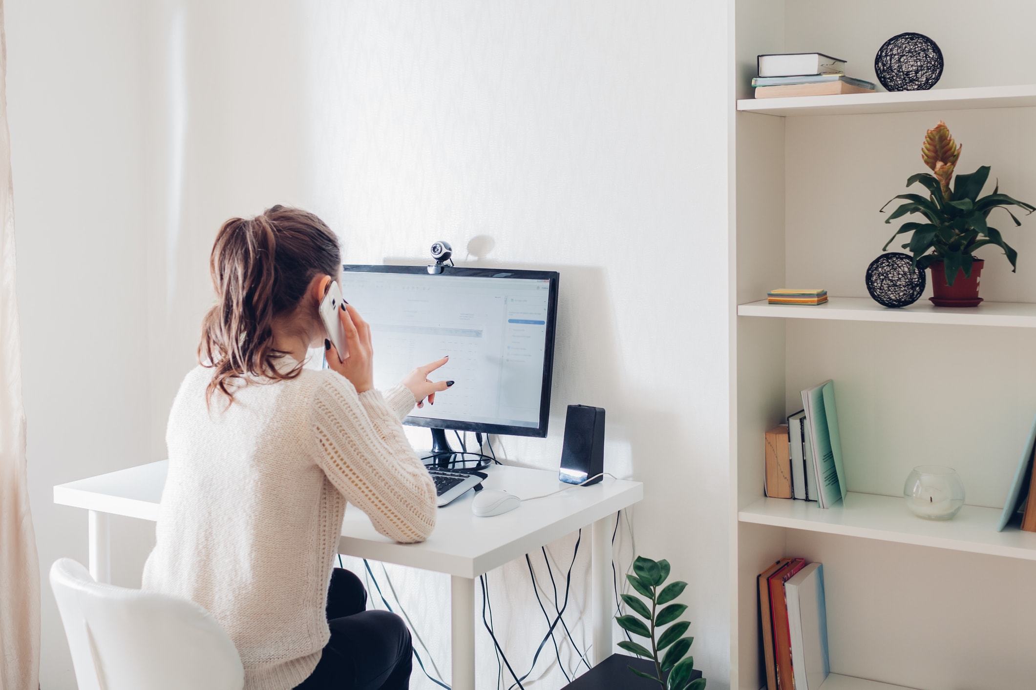 woman pointing at computer screen and talking on cell phone