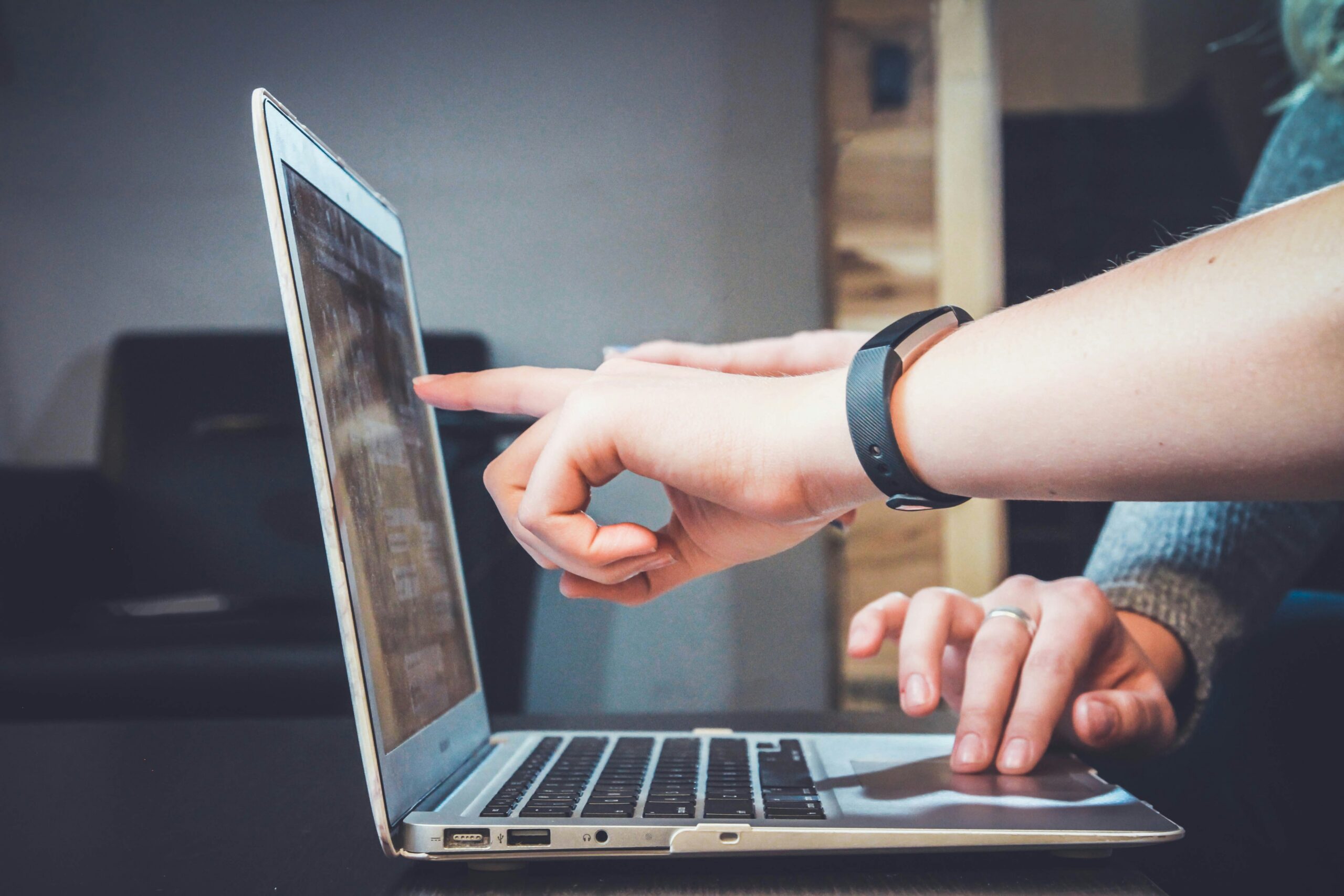 side view of a person's arm pointing at a laptop screen